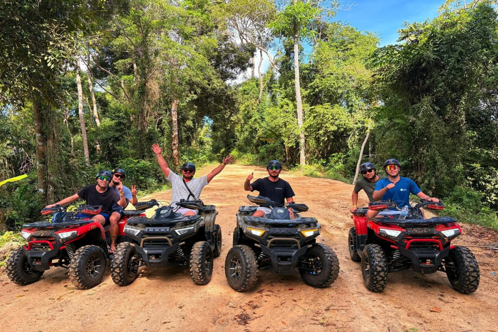 Four quad bikes on a red dirt jungle track on Koh Samui, riders in helmets and sunglasses